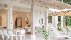 A modern, open-plan living area with a dining table, white chairs, and a lounge area with sun loungers. - Casa Niri, Luxury Villa (Guanacaste Province)