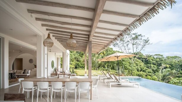 A modern outdoor dining area with a wooden table and white chairs, overlooking a swimming pool and lush greenery. - Casa Niri, Luxury Villa (Guanacaste Province)