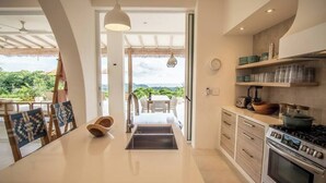 A modern kitchen with a central island, stainless steel appliances, and a view of lush greenery. - Casa Niri, Luxury Villa (Guanacaste Province)