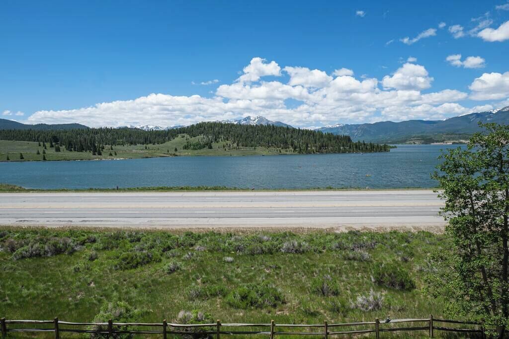 Ein See mit einer Straße im Vordergrund und einem bewaldeten Hügel im Hintergrund.
