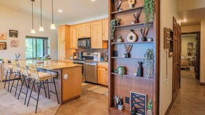 Une cuisine moderne avec des meubles en bois, un îlot central doté de tabourets de bar, un éclairage suspendu et des plantes décoratives.
