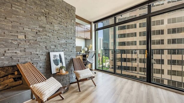 Een modern interieur met een stenen muur, twee houten stoelen, een open haard en een groot raam met uitzicht over de stad.