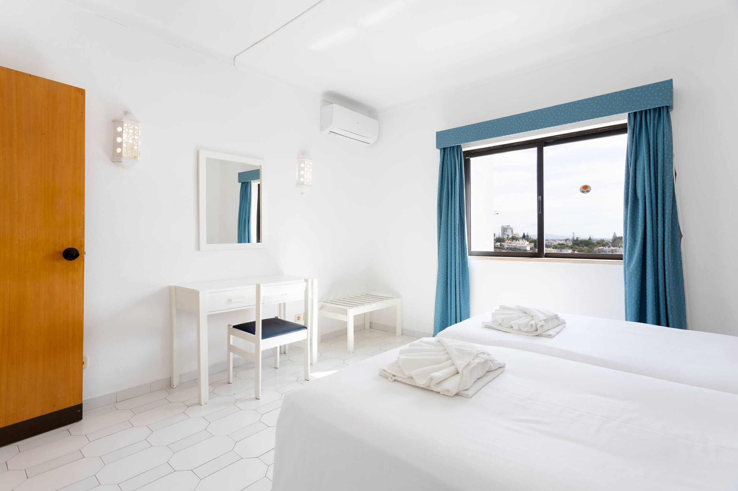 A hotel room with a bed, a desk, a chair, a mirror, and a window with curtains.