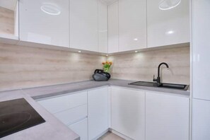 Cozinha moderna com armários brancos, torneira preta e um pequeno vaso com flores na bancada.