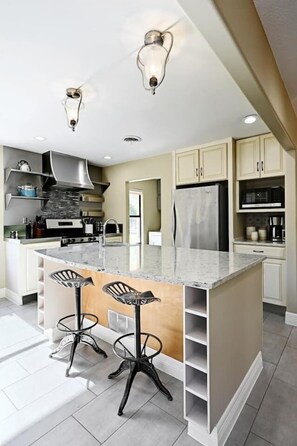 A modern kitchen with a central island, bar stools, stainless steel appliances, and pendant lighting. - Secluded Hill Country Retreat: Bunkhouse and Spa (Austin)
