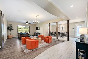 A spacious living room with a large window, a ceiling fan, and a dining area with a view. - Secluded Hill Country Retreat: Bunkhouse and Spa (Austin)