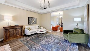 A living room with a white sofa, a coffee table, a patterned rug, a wooden cabinet, and a green armchair. - Secluded Hill Country Retreat: Bunkhouse and Spa (Austin)