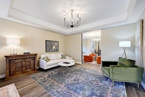 A living room with a white sofa, a coffee table, a patterned rug, a wooden cabinet, and a green armchair. - Secluded Hill Country Retreat: Bunkhouse and Spa (Austin)