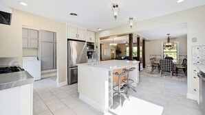 A modern kitchen with a central island, stainless steel appliances, and a dining area with a checkered tablecloth. - Secluded Hill Country Retreat: Bunkhouse and Spa (Austin)