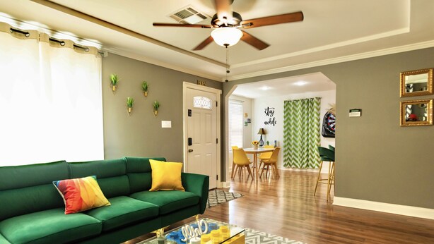 Een moderne woonkamer met een groene bank, een glazen salontafel en een plafondventilator.
