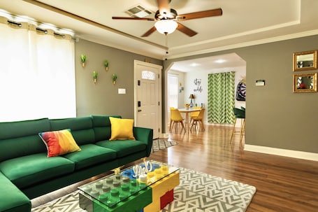 A modern living room with a green sofa, a glass coffee table, and a ceiling fan.