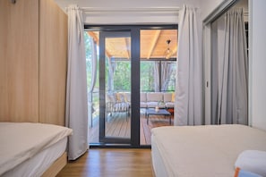 Une chambre avec deux lits, une porte-fenĂȘtre coulissante donnant sur une terrasse extĂ©rieure et une vue sur le paysage.