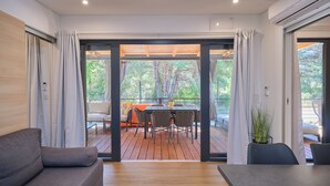 A modern interior with a sofa, dining table, and chairs, a sliding glass door leading to an outdoor deck. - MH Holiday Dream - Morning Sun (Drage)