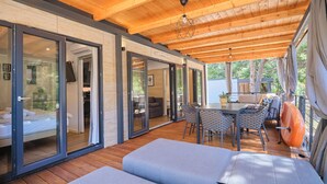 A covered outdoor area with a wooden ceiling, a dining table with chairs, and a sofa. - MH Holiday Dream - Morning Sun (Drage)