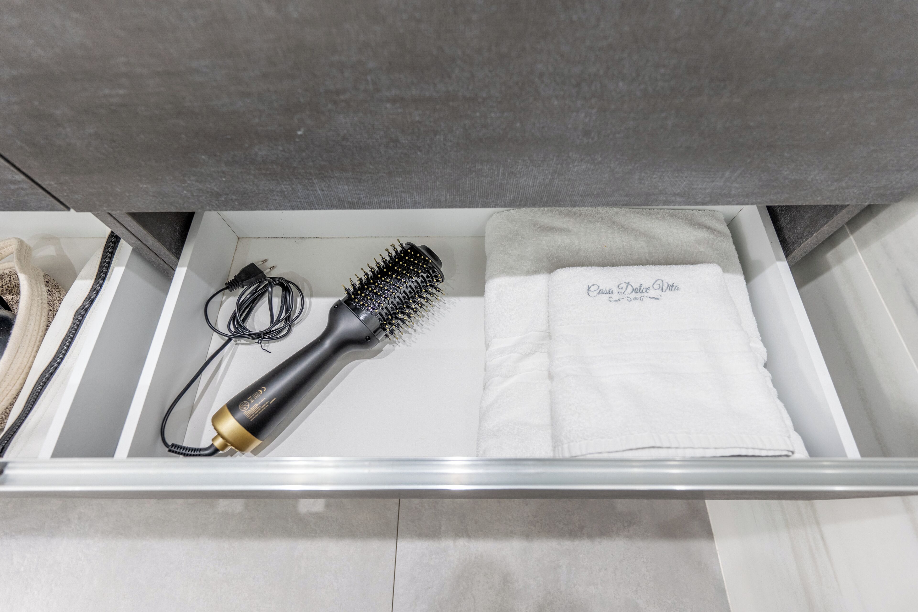 Un tiroir de salle de bain contenant une brosse à cheveux, un sèche-cheveux et une serviette sur laquelle est inscrit « Casa Dolce Vita ».