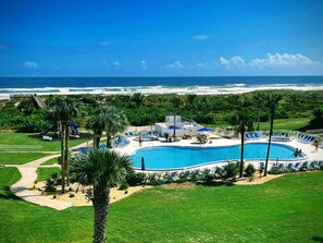 Ein Poolbereich eines Resorts mit Blick auf den Ozean, umgeben von Palmen und einem Spielplatz.