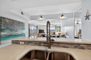 A modern kitchen with a large island, a painting on the wall, and a view to the dining area. - Relaxation Reef - Ocean Views, Heated Pool, Lovely Condo, Beach Access (St. Augustine)