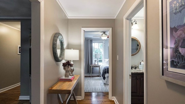 A hallway with a wooden floor, a desk with a lamp, a mirror, and a door leading to a bedroom with a bed and a window. - Five Points Charmer: Delightful 3BR Cottage in Five Points, Complete W/Fire Pit. (Athens)