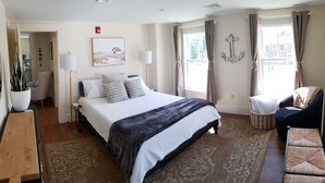 A hotel room with a large bed, a chair, a small table, a potted plant, and a window with curtains.