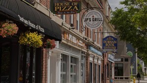 Une vue d’une rue bordée de divers commerces, notamment House of Pizza, Jp’s Grill, Durham Book Exchange et Juicery.
