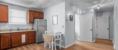 Una cocina moderna con armarios de madera, un refrigerador de acero inoxidable y un comedor con mesa y sillas blancas.