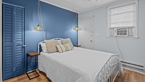 Quarto com cama, mesas de cabeceira, ventoinha no teto e janela com persianas.