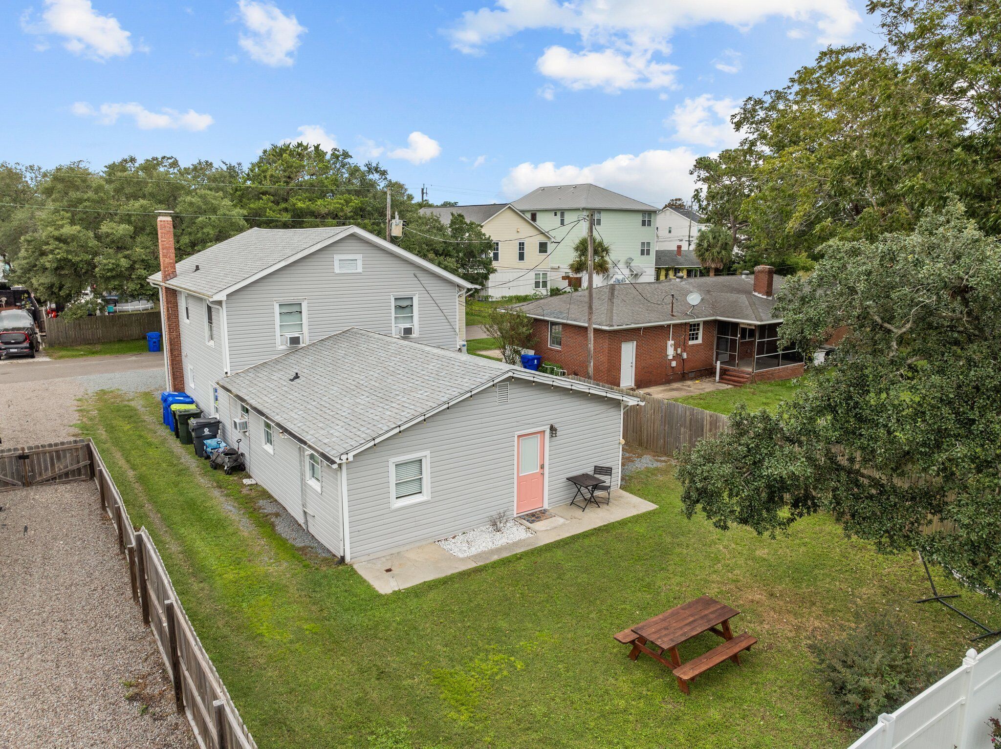 A residential area with a two-story house, a smaller attached garage, and a fenced yard with a picnic table.