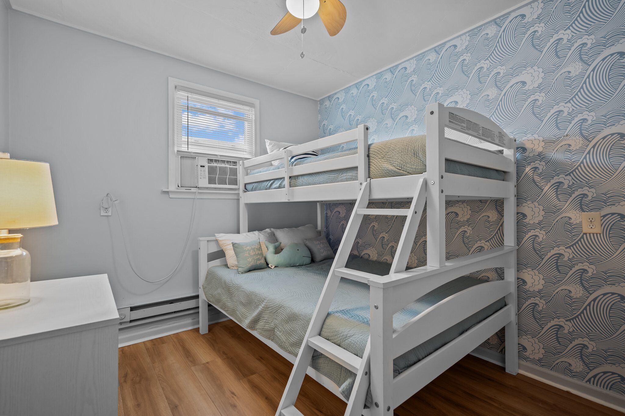 Camera con letto a castello, ventilatore a soffitto, finestra con persiane e carta da parati con motivo a onde.