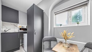 Een kleine keuken met donkere kastjes, een ingebouwde magnetron en een raam met uitzicht op bomen.