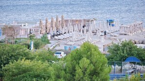 Et hotel ved stranden med rækker af hvide liggestole og parasoller, et poolområde og udsigt til havet.