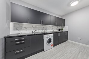 Une cuisine moderne avec des meubles de couleur sombre, un lave-linge encastré et un pare-feu en marbre.