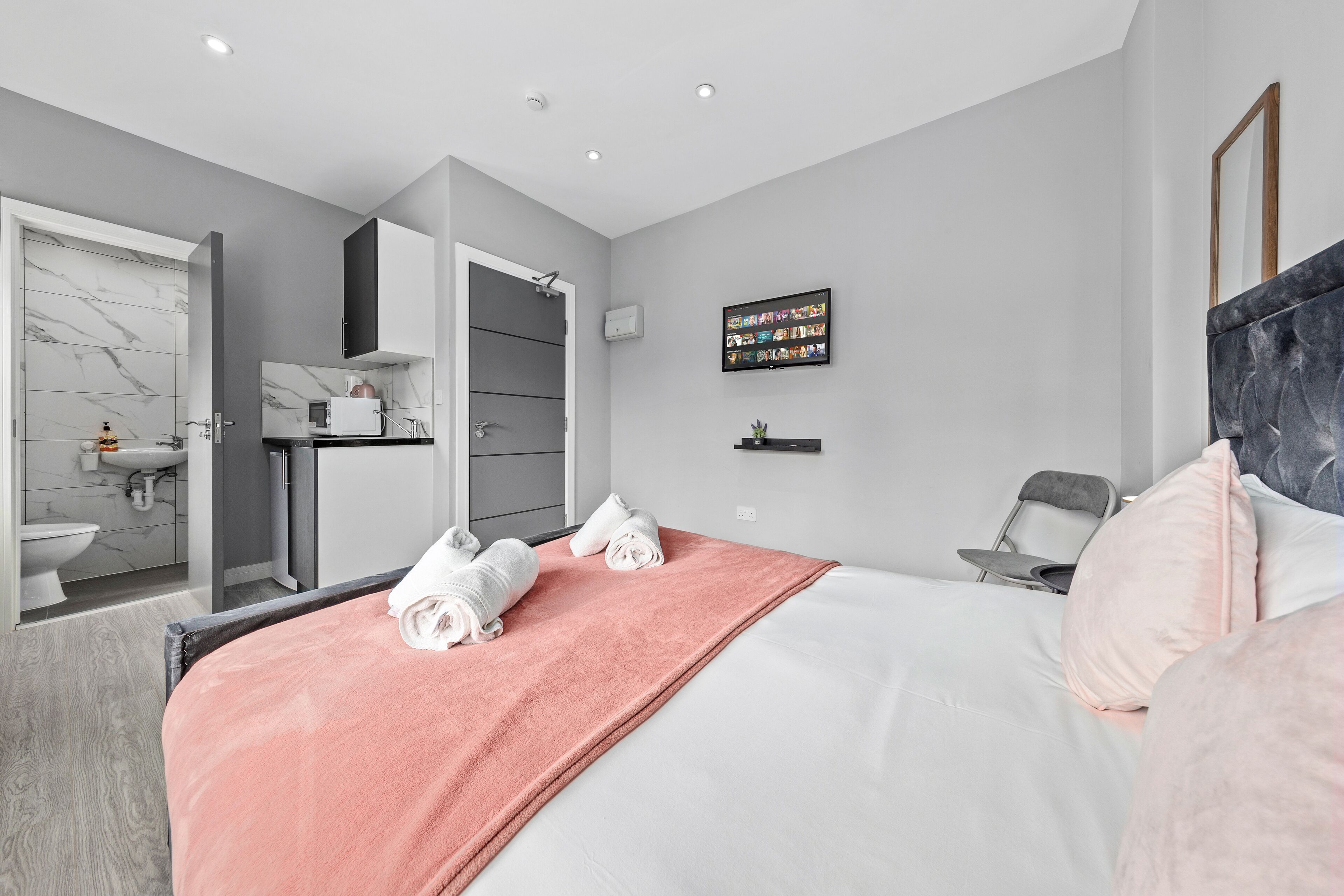 Et moderne hotelværelse med en pænt redt seng, et badeværelse med marmorbeklædning og et fladskærms-tv ophængt på væggen.