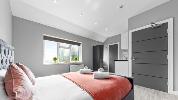Un dormitorio moderno con cama, paredes grises, un ventanal y un armario.