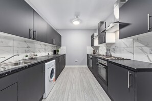 Une cuisine moderne avec des meubles gris, un lave-linge encastré et un pare-feu en marbre.
