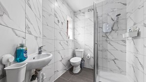 Ein modernes Badezimmer mit Marmorfliesenspiegel, einem weißen Waschbecken mit Seifenspender, einer Toilette und einer Duschkabine.