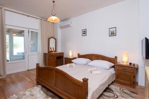 Quarto com cama de madeira, luminárias de cabeceira, espelho e televisão na parede.