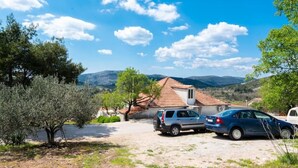 Una casa rurale con tetto in tegole, auto parcheggiate e una vista chiara delle colline circostanti.