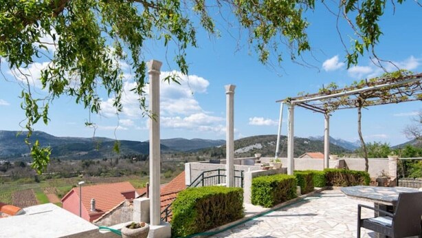 Una terrazza con pavimento in pietra, un pergolato e vista su colline lontane.