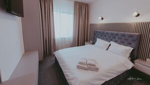 A hotel room with a large bed, a flat-screen TV mounted on the wall, a bedside table, and a window with curtains. - BELVEDERE  (Baia de Fier)