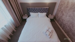 A neatly made bed with white linens, a tufted headboard, and two bedside lamps. - BELVEDERE  (Baia de Fier)