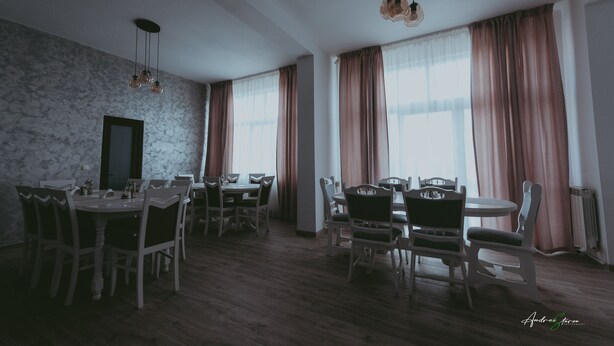 A dining area with wooden tables and chairs, large windows with curtains, and hanging pendant lights. - BELVEDERE  (Baia de Fier)