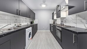Une cuisine moderne avec des meubles gris, un lave-linge encastré et un pare-feu en marbre.