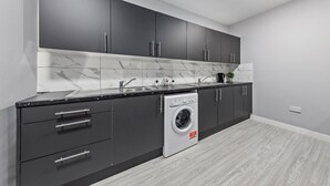 Une cuisine moderne avec des meubles de couleur sombre, un lave-linge encastré et un pare-feu en marbre.