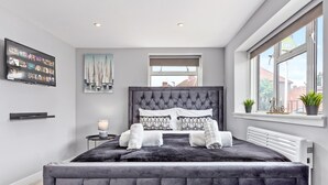 Une chambre moderne avec un grand lit, un téléviseur à écran plat, un tableau et une fenêtre donnant sur des immeubles.