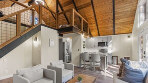 Un'ampia zona giorno con soffitto alto, travi in legno e una cucina sullo sfondo.