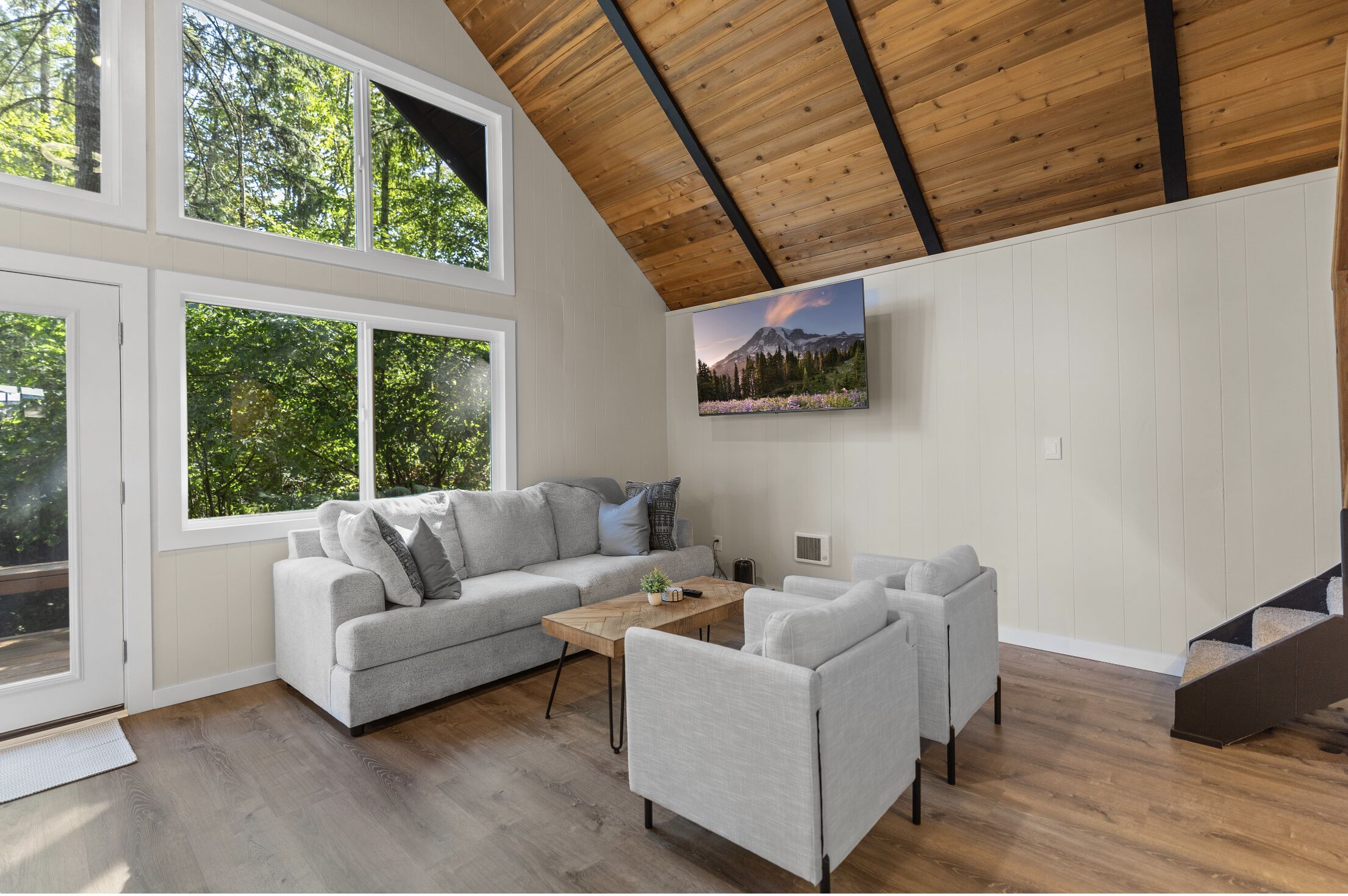 A modern living room with a grey sofa, two armchairs, a wooden coffee table, and a painting of a mountain landscape.
