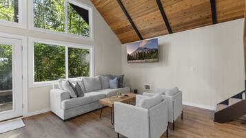 A modern living room with a grey sofa, two armchairs, a wooden coffee table, and a painting of a mountain landscape.
