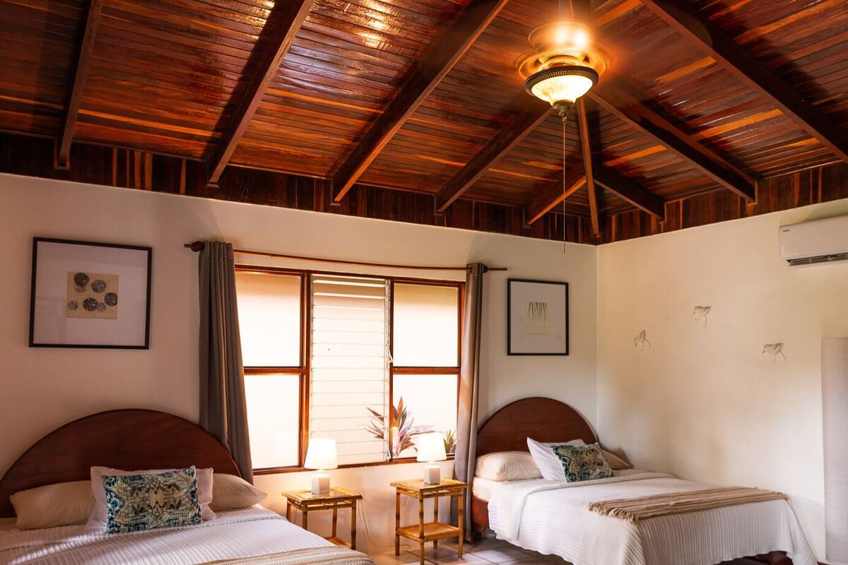 A bedroom with two beds, a wooden ceiling, and a window with curtains.