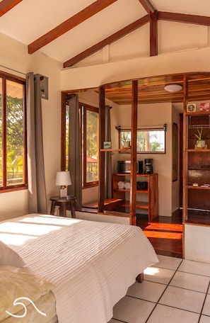 Un dormitorio con una cama grande, vigas de madera, un escritorio con lámpara y vistas al exterior.