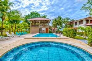 A pool area with a wooden deck, lounge chairs, and a covered seating area.